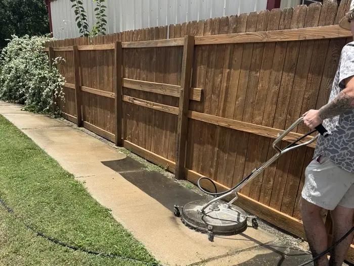 Worker pressure washing a concrete sidewalk.